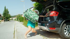 Woman stuffing luggage into trunk of a car